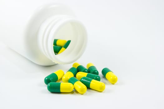 Green and yellow pills out of bottle on white background