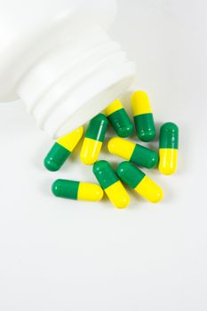 Green and yellow pills out of bottle on white background with copyspace