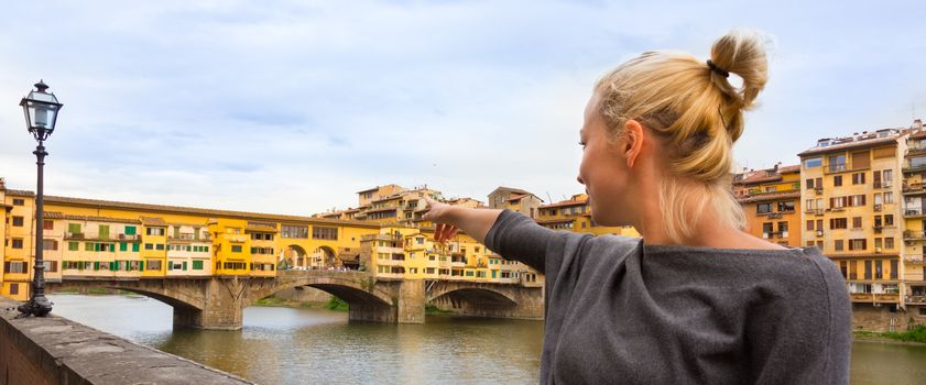 Young lady pointing on Ponte Vecchio bridge in Florence, Tuscany, Italy, during her summer vacations in Europe.