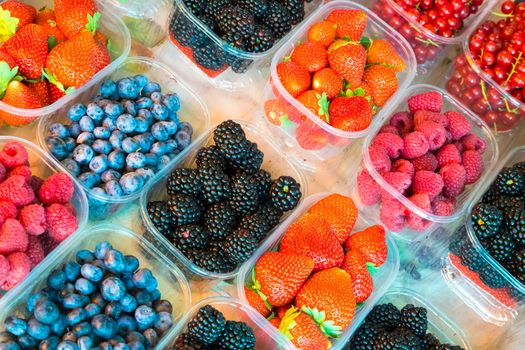 Blueberries, raspberries, strawberries, currants and blackberries in boxes formin colourful pattern.