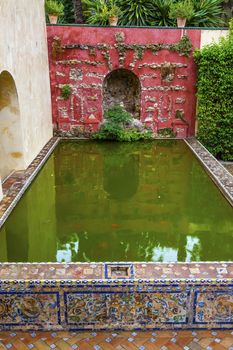 Green Pool Basin Reflection Mosaic Wall Garden Alcazar Royal Palace Seville Andalusia Spain.  Originally a Moorish Fort, oldest Royal Palace still in use in Europe. Built in the 1100s and rebuilt in the 1300s. 