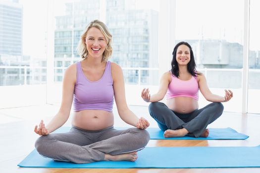 Smiling pregnant women in yoga class in lotus pose in a fitness studio