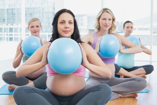 Happy pregnant women in yoga class holding medicine balls in a fitness studio