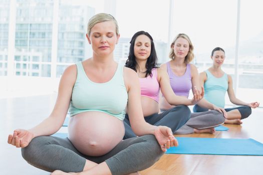 Pregnant women in yoga class sitting on mats with eyes closed in a fitness studio