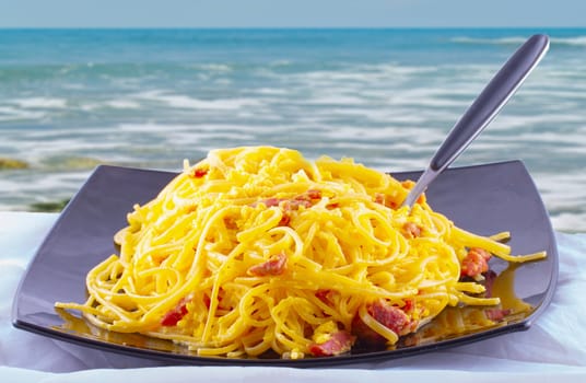 Pasta alla carbonara with sea on the background