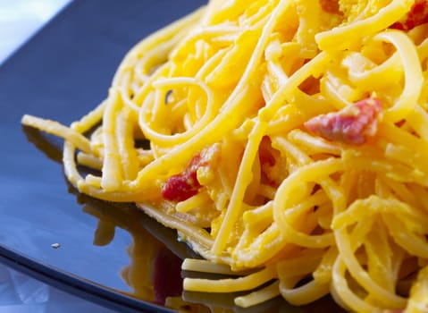 Pasta alla carbonara in close up, over black reflecting plate