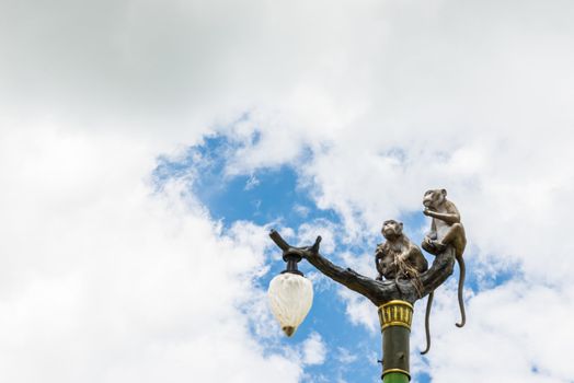 Statue of a monkey family on lamp post on blue sky and clouds.