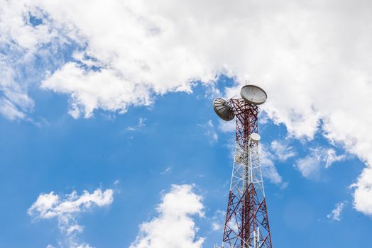 Red and white tower of communications with a lot of different antennas under clear sky.