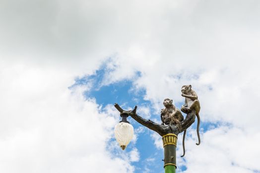 Statue of a monkey family on lamp post on blue sky and clouds.