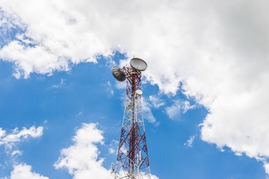 Red and white tower of communications with a lot of different antennas under clear sky.