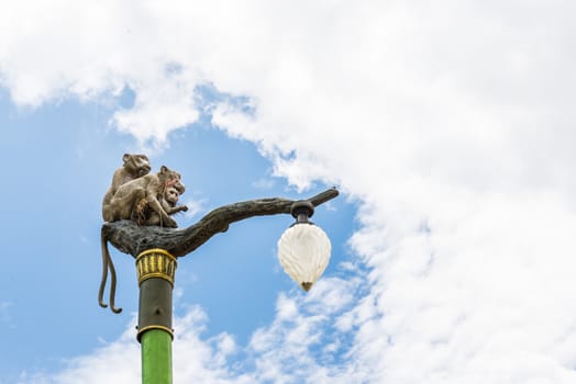 Statue of a monkey family on lamp post on blue sky and clouds.