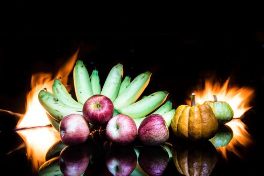 still life color-full little pumpkins and banana and apple on black glass on fire and black background