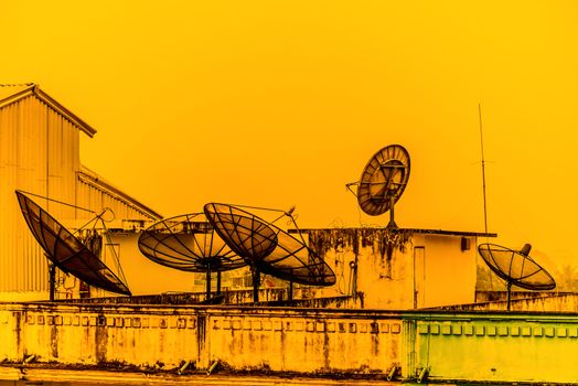 A few satellite dishes on a roof in the sunset