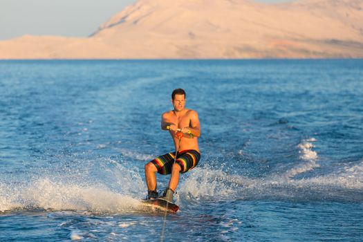 Wakeboarder in colorful shorts riding in sunset.