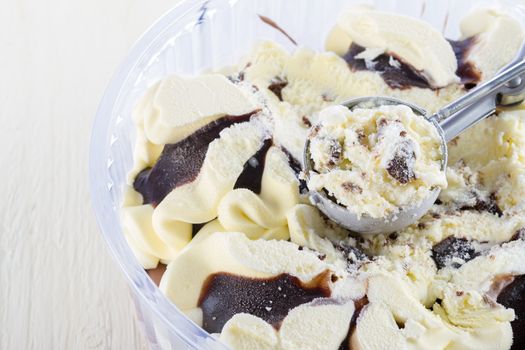 Vanilla with chocolate ice cream scoop scooped out of a container on white wooden background