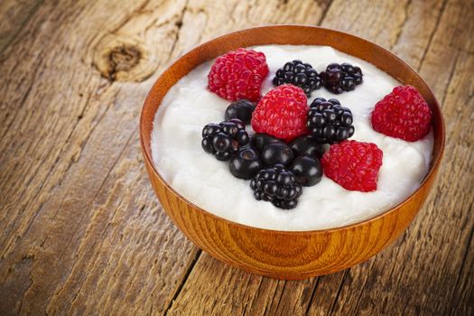 Yogurt with berries in wooden bowl on wooden background