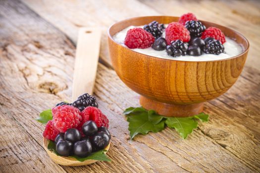 yogurt with wild berries in wooden bowl on wooden background