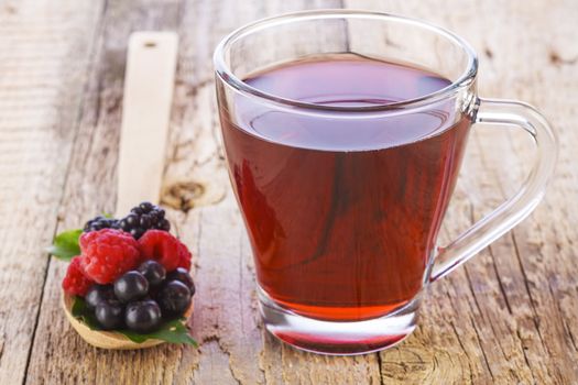 Fruit red tea with wild berries in wooden spoon on brown wooden table