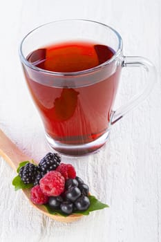 Fruit red tea with wild berries in wooden spoon on white wooden table