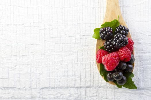 Fresh berries in wooden spoon on white wooden table