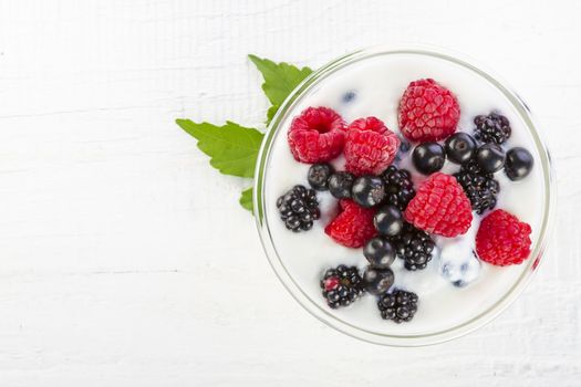 Yogurt with forest berries in bowl on white wooden table