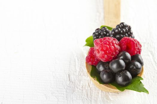 Fresh berries in wooden spoon on white wooden table