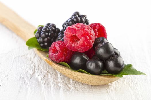 Fresh berries in wooden spoon on white wooden table