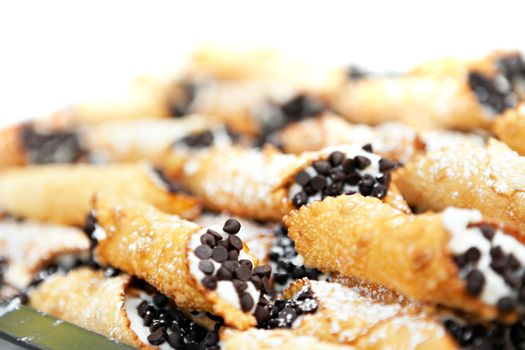 Tray full of freshly filled cannolis with chocolate chips and confectioners sugar. Shallow depth of field.