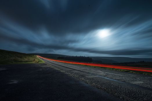 Blur light in night shoot of fast driving car with blurred clouds over full super moon and road