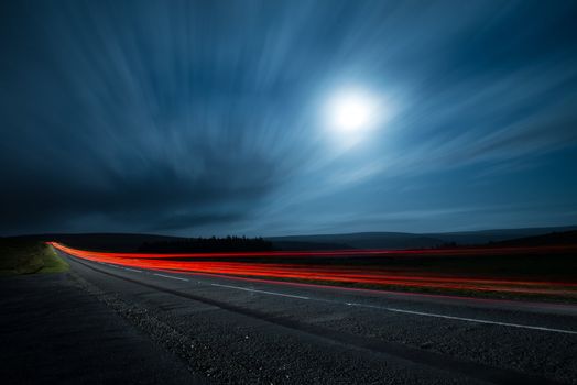 Blur light in night shoot of fast driving car with blurred clouds over full super moon and road