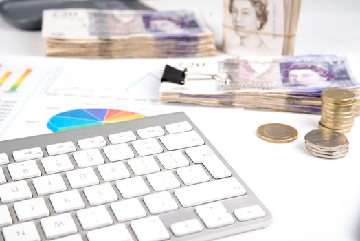 British pound sterling coins and bank notes on desk with keyboard and financial chart