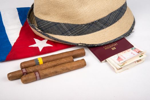 Cuban cigars and hat with passport and cuban currency pesos over Cuban national flag on white isolated background