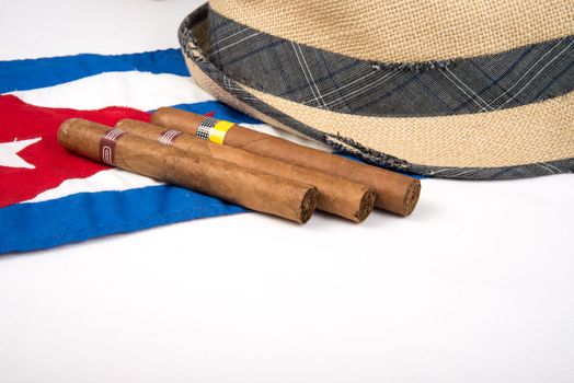 Cuban cigars and hat over Cuban national flag on white isolated background