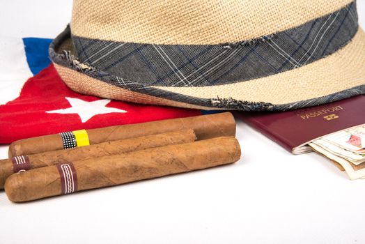 Cuban cigars and hat with passport and cuban currency pesos over Cuban national flag on white isolated background