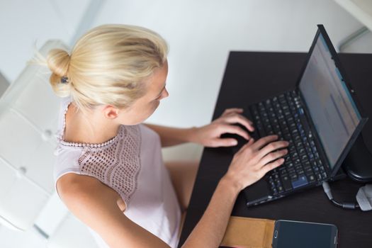Business woman, casualy dressed, typing ona a leptop computer, working from her home.