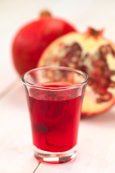 Grenadine syrup in shot glass with pomegranate in the back (Selective Focus, Focus on the front rim of the glass)