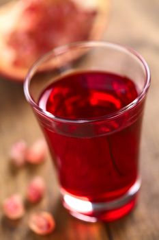 Grenadine syrup in shot glass with pomegranate seeds on the side and pomegranate in the back (Selective Focus, Focus on the front rim of the glass)