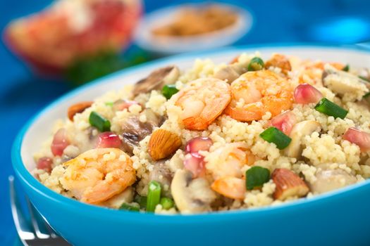Couscous dish with shrimps, mushroom, almond, pomegranate seeds and green onion served in blue bowl (Selective Focus, Focus on the tails of the shrimps on the top of the meal) 