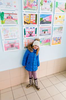 Cute girl near wall with children drawings