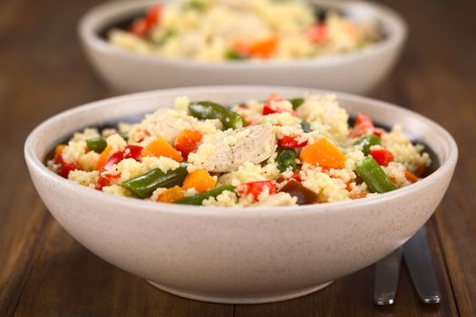 Two bowls of couscous dish with chicken, green bean, carrot and red bell pepper (Selective Focus, Focus on the chicken meat in the middle of the image) 