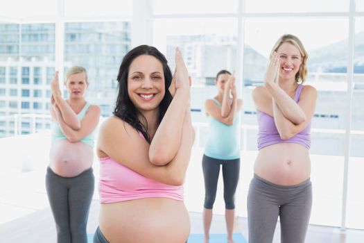 Happy pregnant women in yoga class standing in eagle pose in a fitness studio