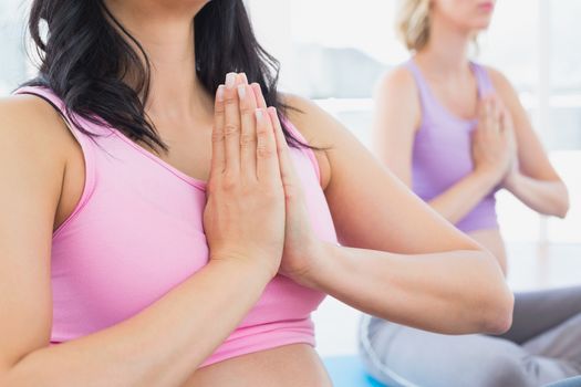 Meditating pregnant women at yoga class in lotus pose in a fitness studio