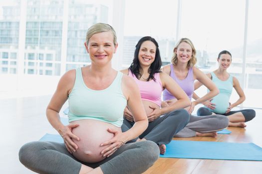 Pregnant women in yoga class sitting on mats touching their bumps in a fitness studio