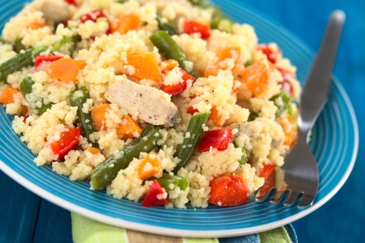 Couscous dish with chicken, green bean, carrot and red bell pepper served on plate with fork on the side (Selective Focus, Focus on the meat in the middle of the image) 