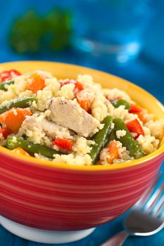 Couscous dish with chicken, green bean, carrot and red bell pepper in colorful bowl on blue wood (Selective Focus, Focus one third into the dish) 