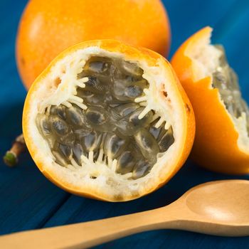 Sweet granadilla or grenadia (lat. Passiflora ligularis) fruit cut in half,  of which the seeds and the surrounding juicy pulp is eaten or is used to prepare juice, with wooden spoon in the front (Selective Focus, Focus on the front of the seeds)