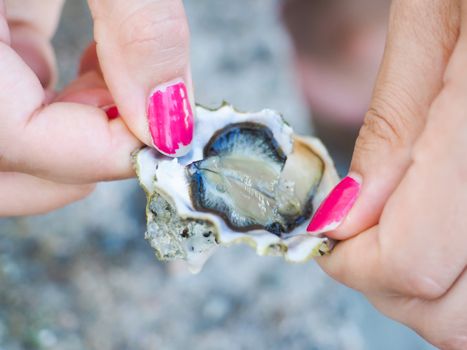 Female person holding an oyster mussel wide open with pink nail paint