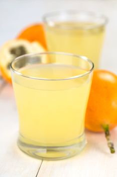 Fresh juice made of sweet granadilla or grenadia (lat. Passiflora ligularis) in glass with granadilla fruit in the back (Selective Focus, Focus on the front rim of the glass)