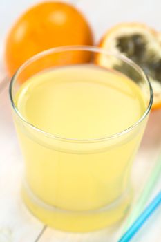 Fresh juice made of sweet granadilla or grenadia (lat. Passiflora ligularis) in glass with straws on the side and granadilla fruit in the back (Selective Focus, Focus on the front rim of the glass)