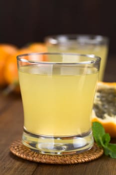 Fresh juice made of sweet granadilla or grenadia (lat. Passiflora ligularis) in glass with granadilla fruit in the back (Selective Focus, Focus on the front rim of the glass)